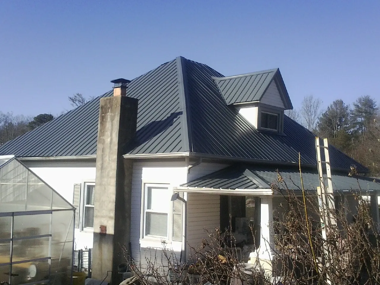 Dark blue standing seam metal roof on a white farmhouse with dormer — Slate & Tile Roof Repair by Roofing Brothers in Velma