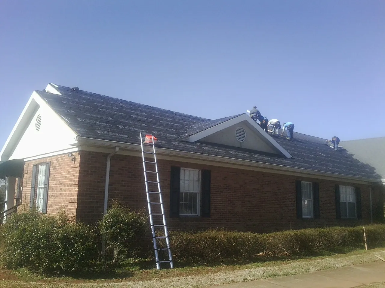 Crew tearing shingles off a brick ranch roof with a ladder set — Emergency Roof Repair work by our crew in Velma
