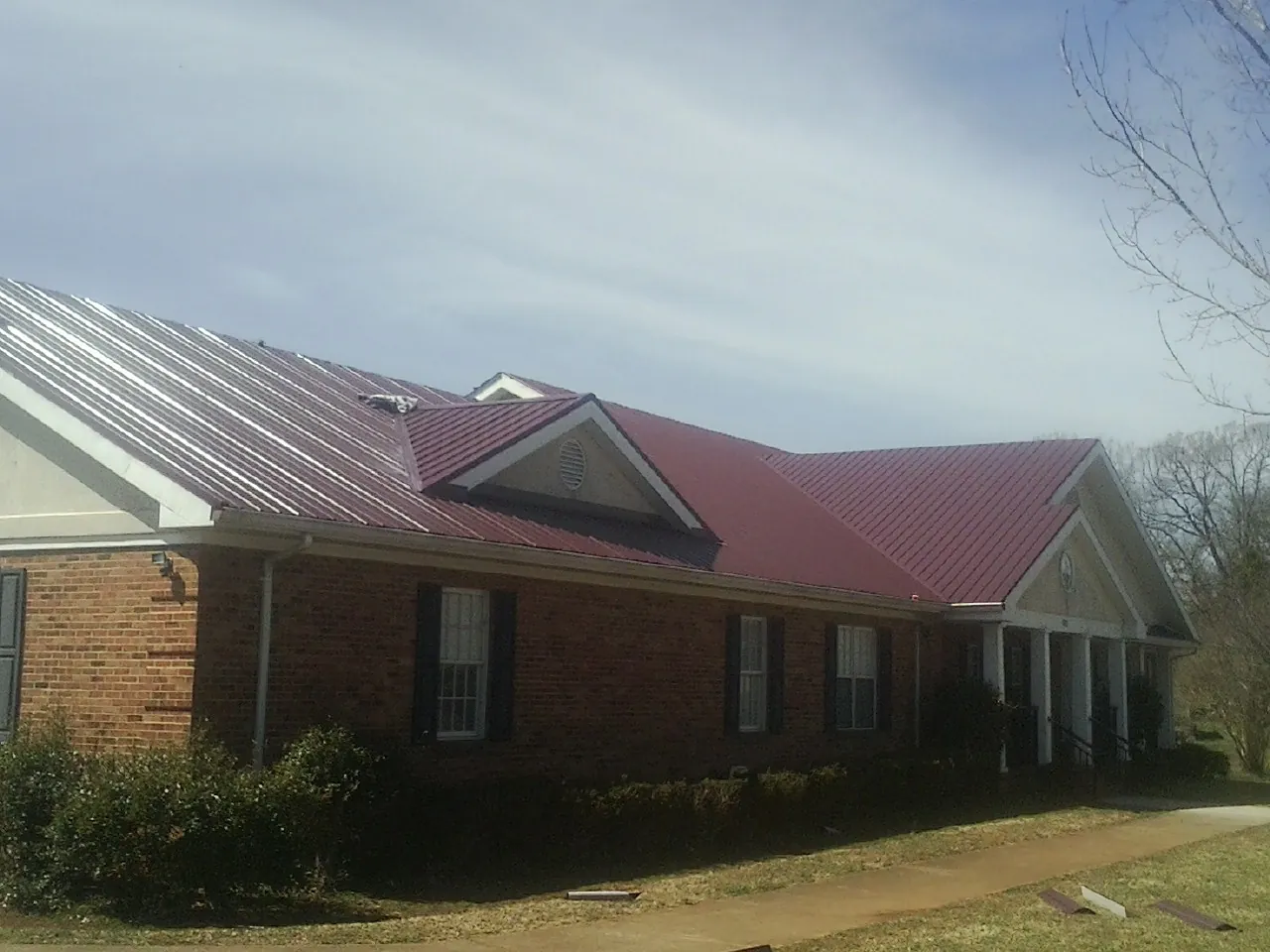 Red metal roof with gabled entries on a long brick building, from a Hail Damage Roof Repair job in Velma