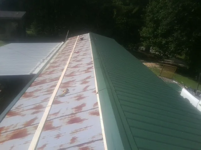 Old rusted panels beside newly installed green metal roofing — Wind Damage Roof Repair by Roofing Brothers in Velma