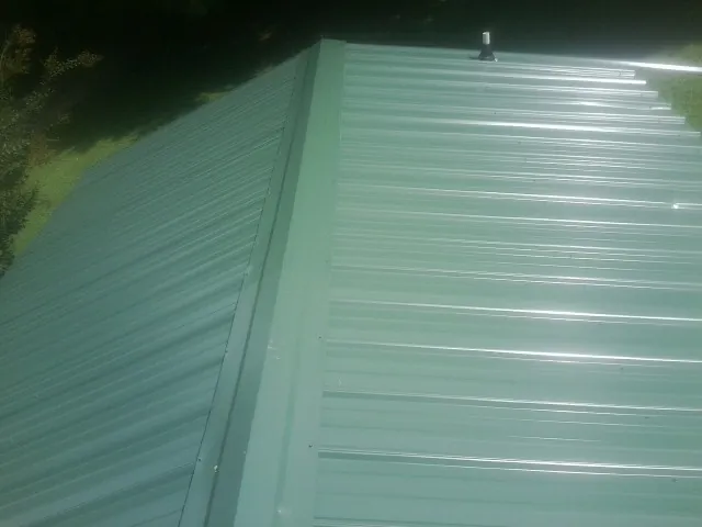 New green metal panels meeting at the ridge of a roof — Flat Roof Repair work by our crew in Velma