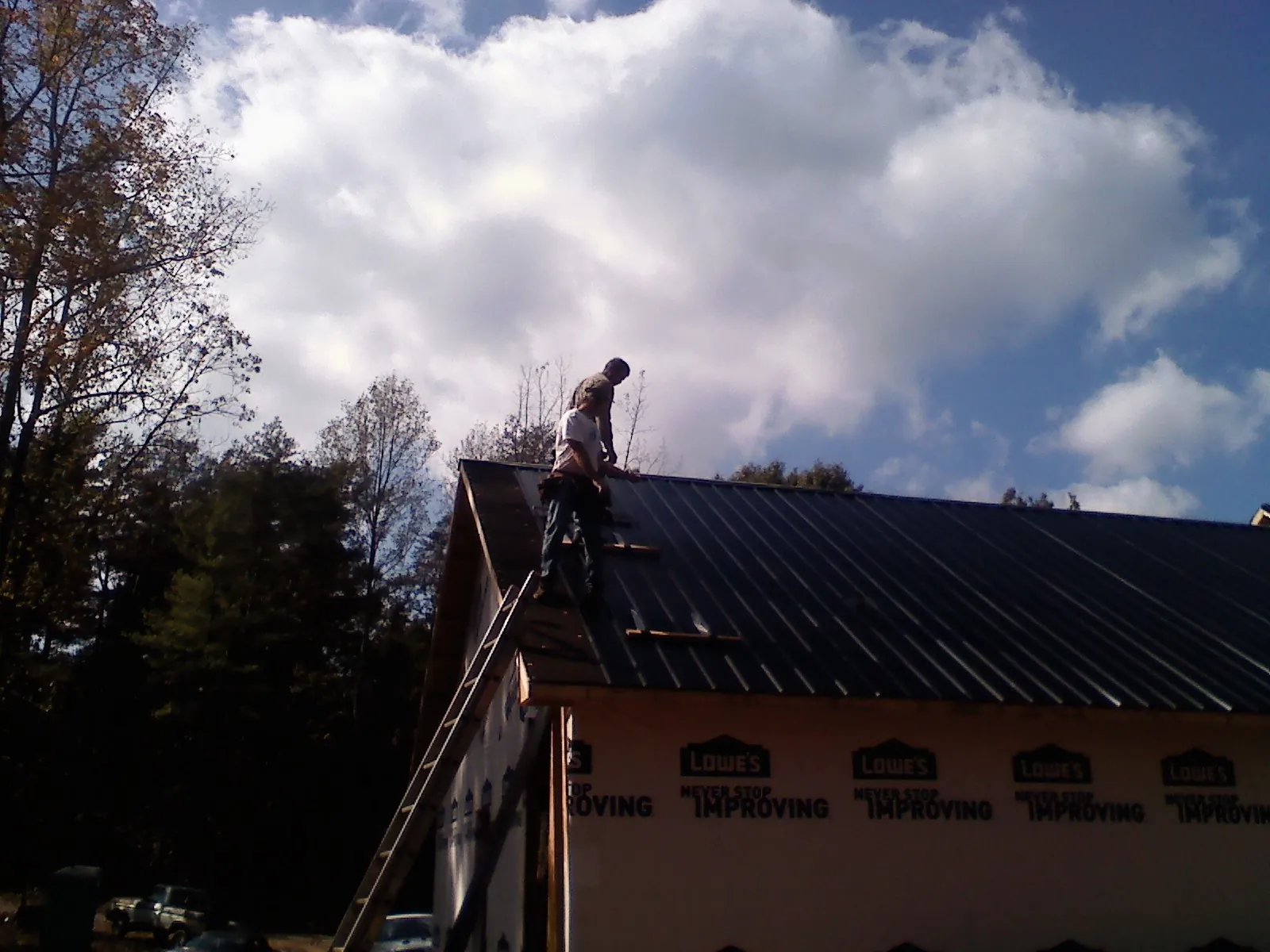 Roofer fastening dark metal panels high against a cloudy sky in Velma