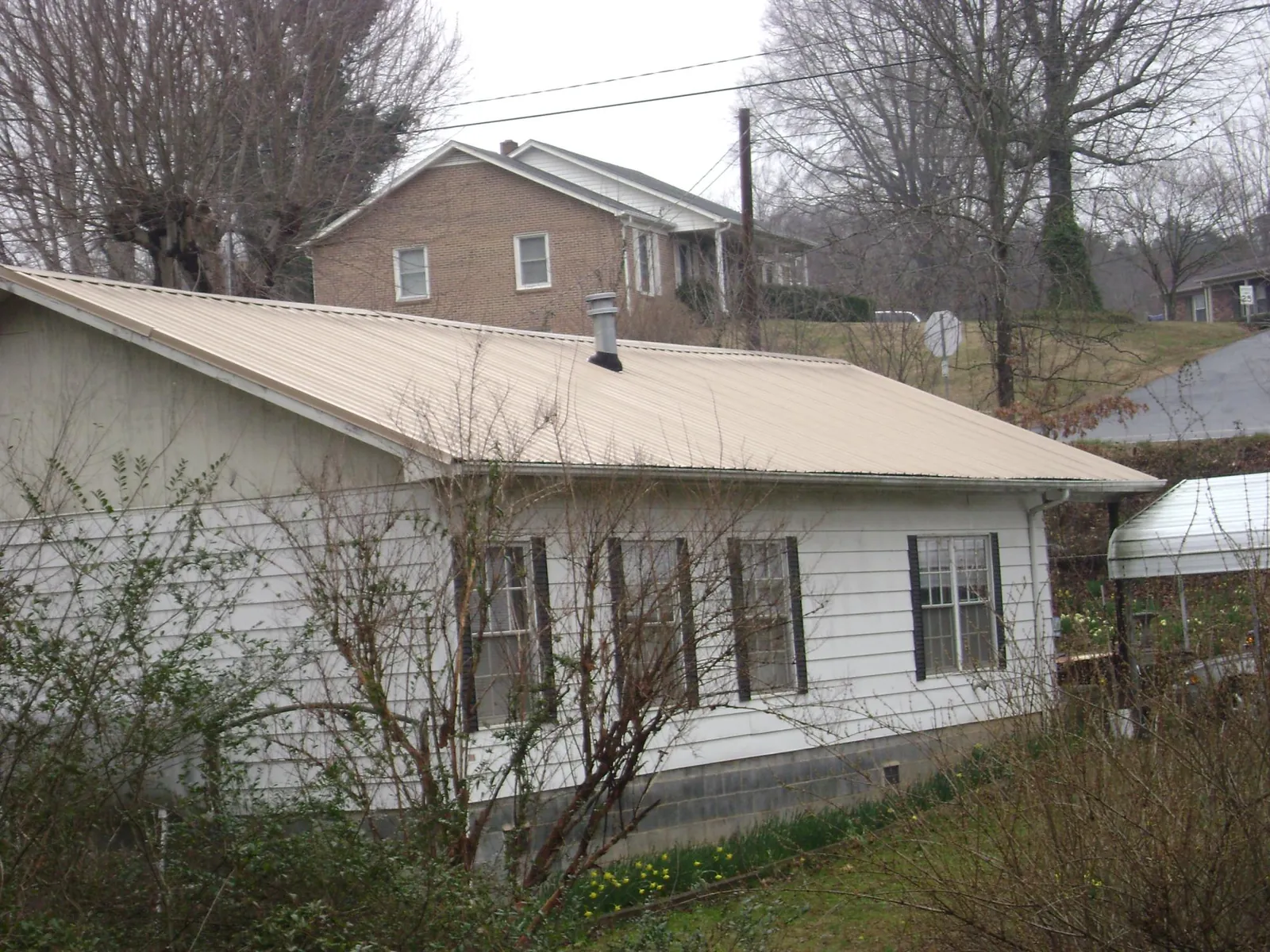 Tan metal roof on a white sided house set into a hillside — Commercial Roofing by Roofing Brothers in Velma