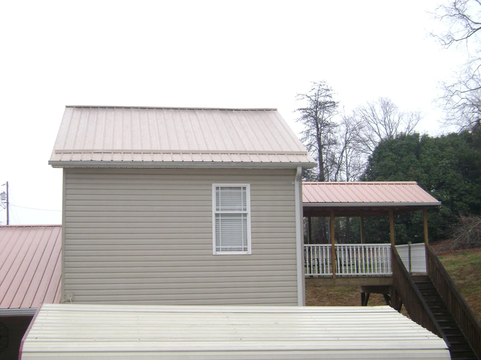 Tan metal roofs on a two story addition and attached porch, from a Roof Replacement job in Velma