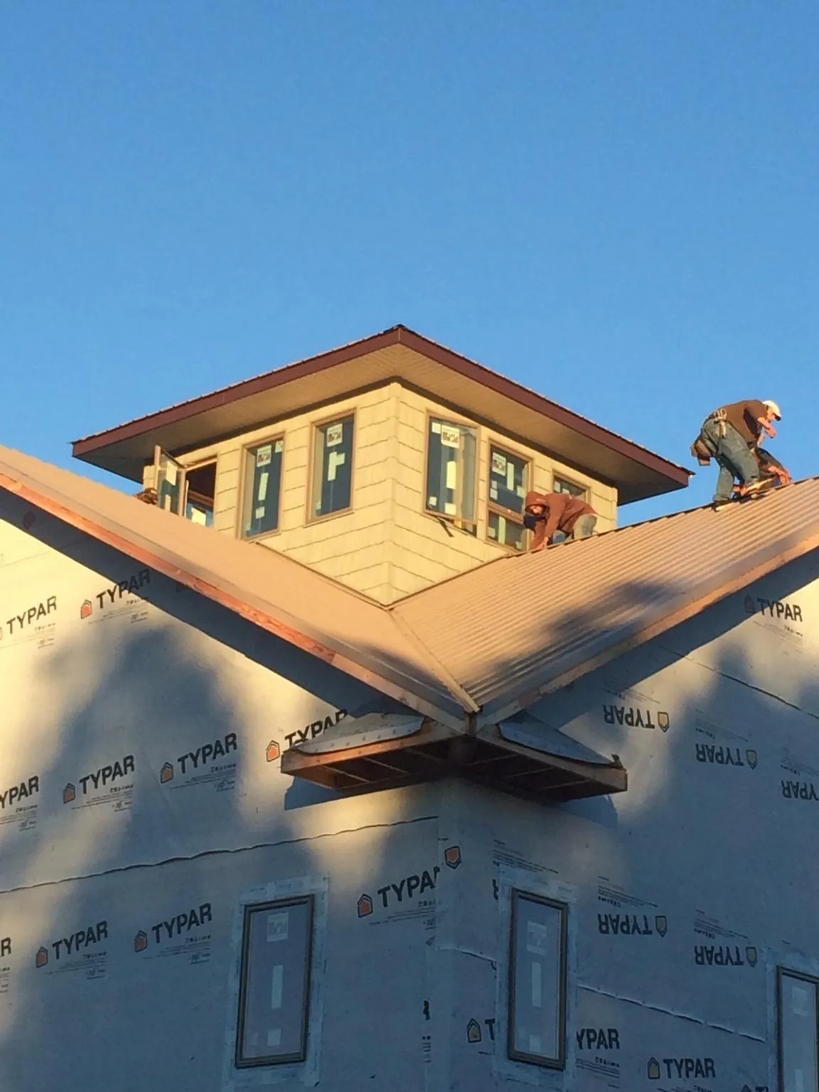 Roofers working around a rooftop cupola on a new metal roof at sunset — Roof Waterproofing in Velma by Roofing Brothers
